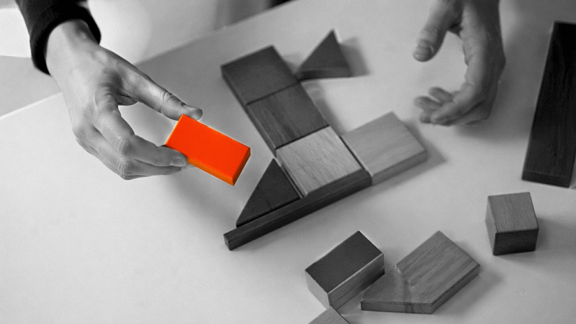 Hand bewegt einen orangen Holzklotz in eine neue Position